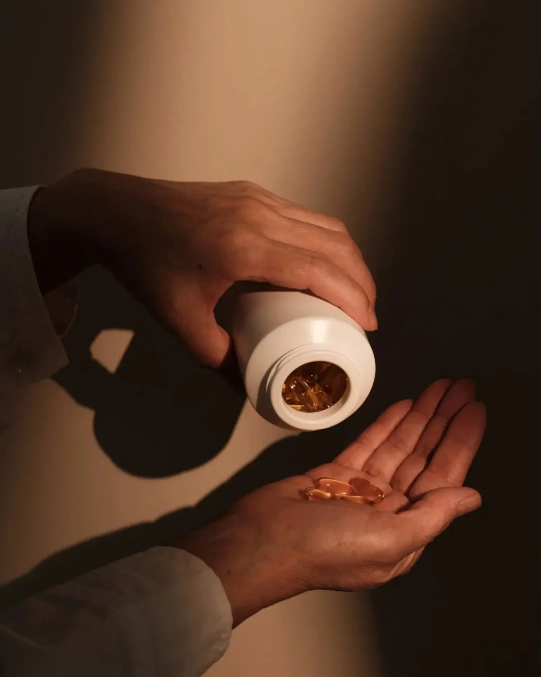 Mains versant des capsules dorées translucides depuis un flacon blanc, illustrant la transparence totale d'atout santé nature, la pureté et le clean label de nos compléments alimentaires. Image