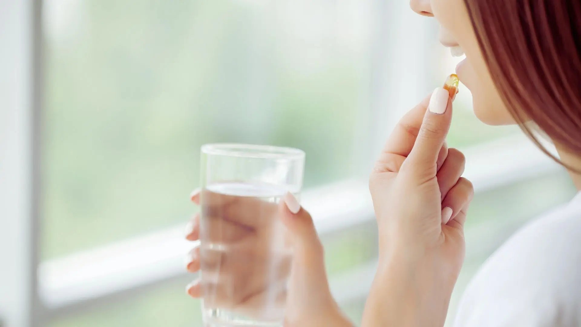 Femme prenant une gélule de complément alimentaire avec un verre d'eau, illustrant l'absorption et la biodisponibilité des nutriments Image